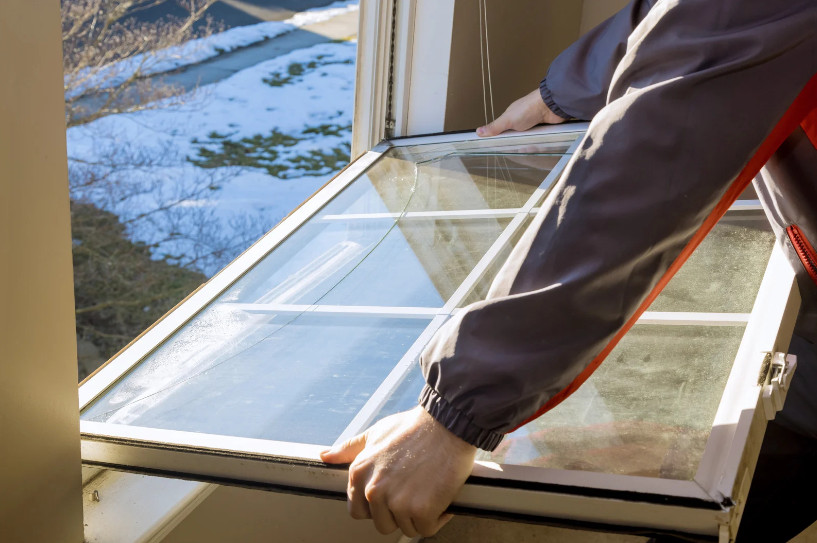 A skilled technician is installing a new window on a residential home, aligning the frame and securing it with precision tools. He is wearing protective gear and working on a well-maintained house in a suburban neighborhood. The scene reflects the professional quality of window replacement in Arlington, TX, with attention to energy efficiency, proper sealing, and clean installation.