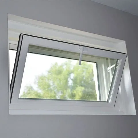A white tilt-and-turn window is partially open inwards, set in a light gray wall. Green trees and a blue sky are visible through the window.