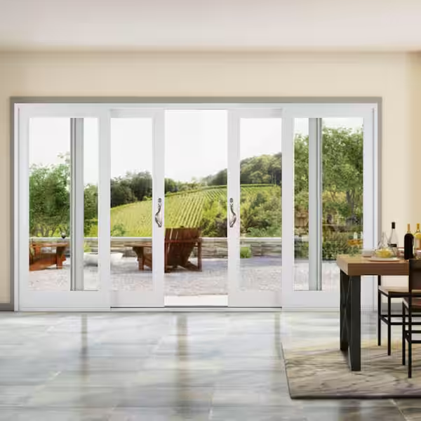 Large glass patio doors open to a terrace with wooden chairs and a view of a vineyard. Inside, there is a dining table with wine bottles, glasses, and a plant. The scene is bright and inviting.