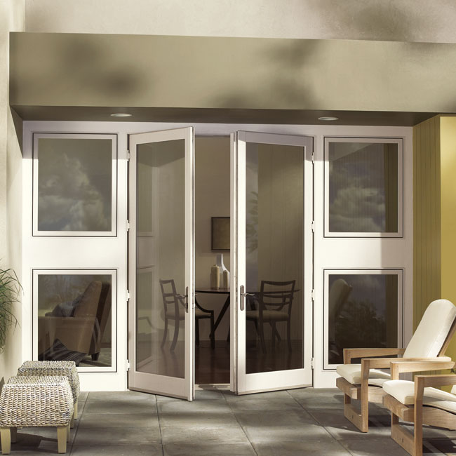 A set of white folding glass patio doors is partially open, leading from a tiled outdoor area with chairs into an indoor space with a table and chairs. Four large glass windows surround the doors.